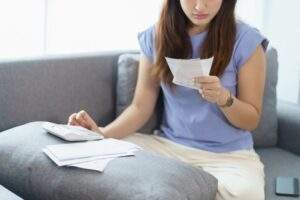 一名女性坐在沙發上認真核對收據與帳單，進行每月的財務審核與儲蓄計畫管理。